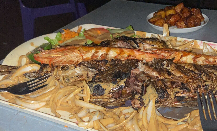 A Senegalese platter with grilled fish, shrimp, plantain, and onion sauce enjoyed on the beach.
