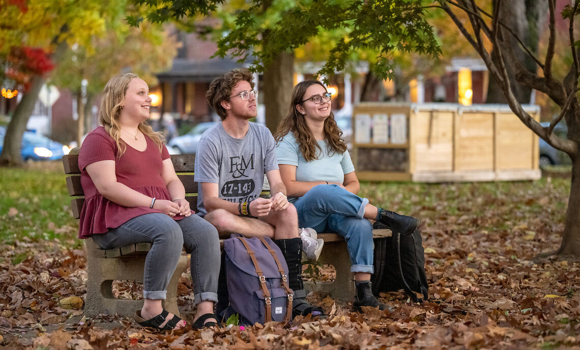 Caroline Kleis 24, Bennett Wasch 23, and Athena Kotsopriftis 25 discuss their involvement with Lancaster Composting Co-Ops. The Buchanan Park compost bin can be seen in the background.